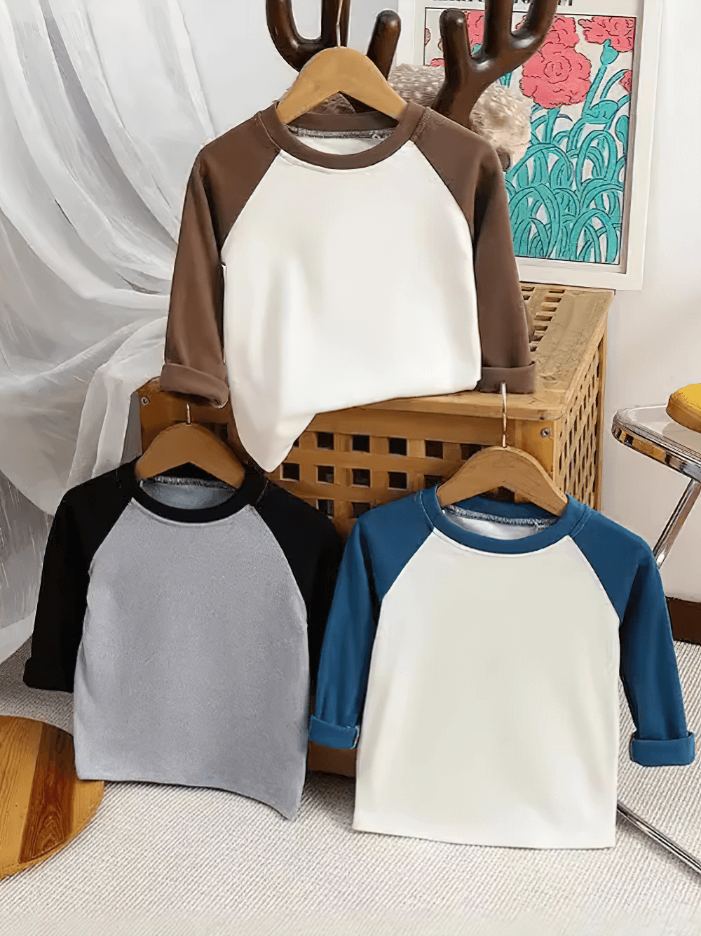 Three cute raglan sleeve tops for kids with round necks in brown, black, and blue colors, displayed on hangers.